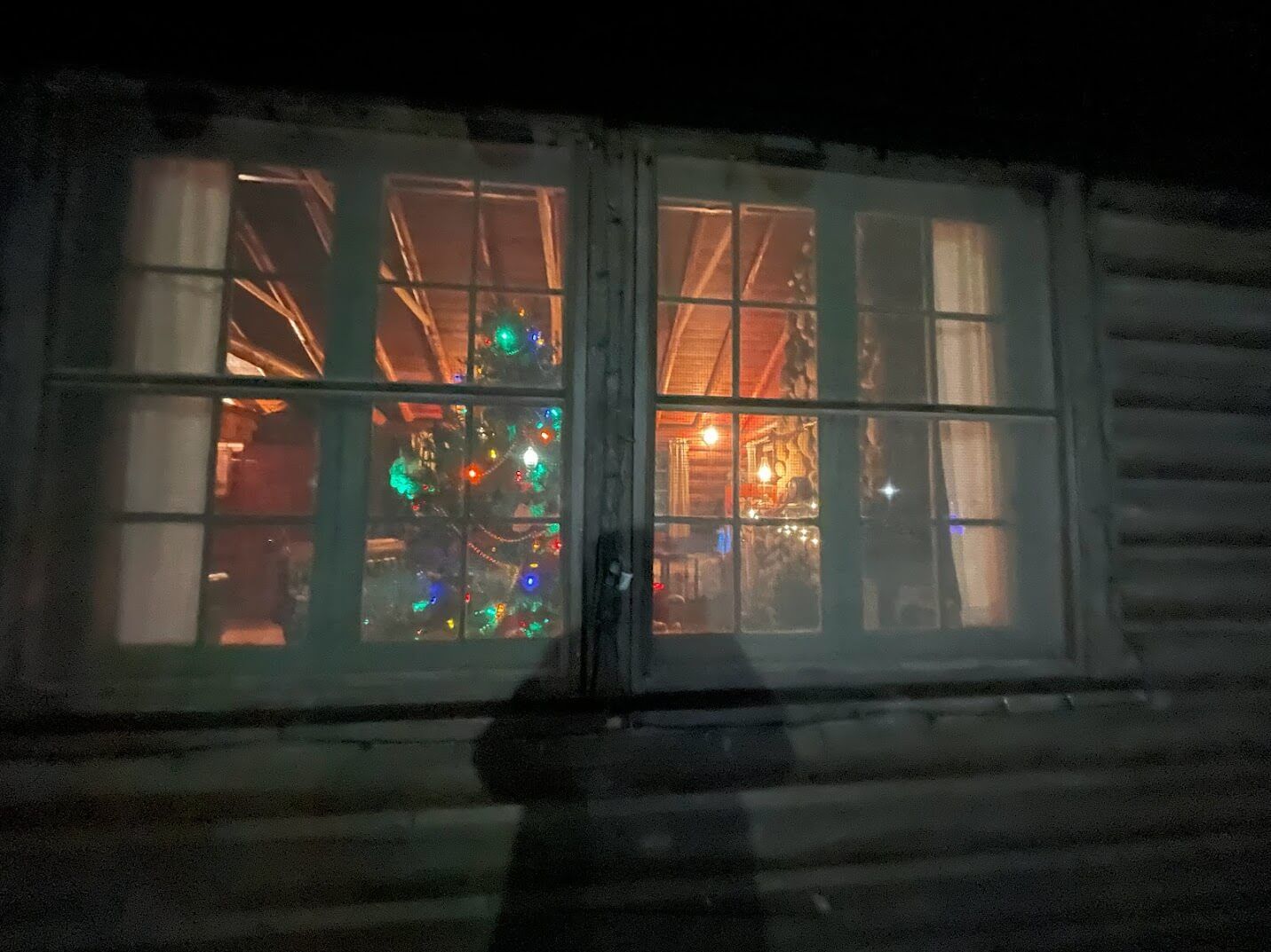 A christmas tree is lit up in the window of a log cabin