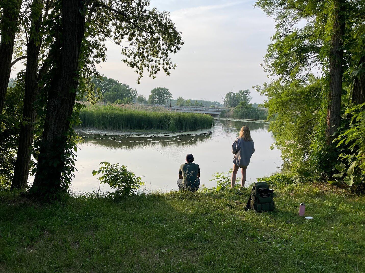 Two people are sitting on the shore of a lake.