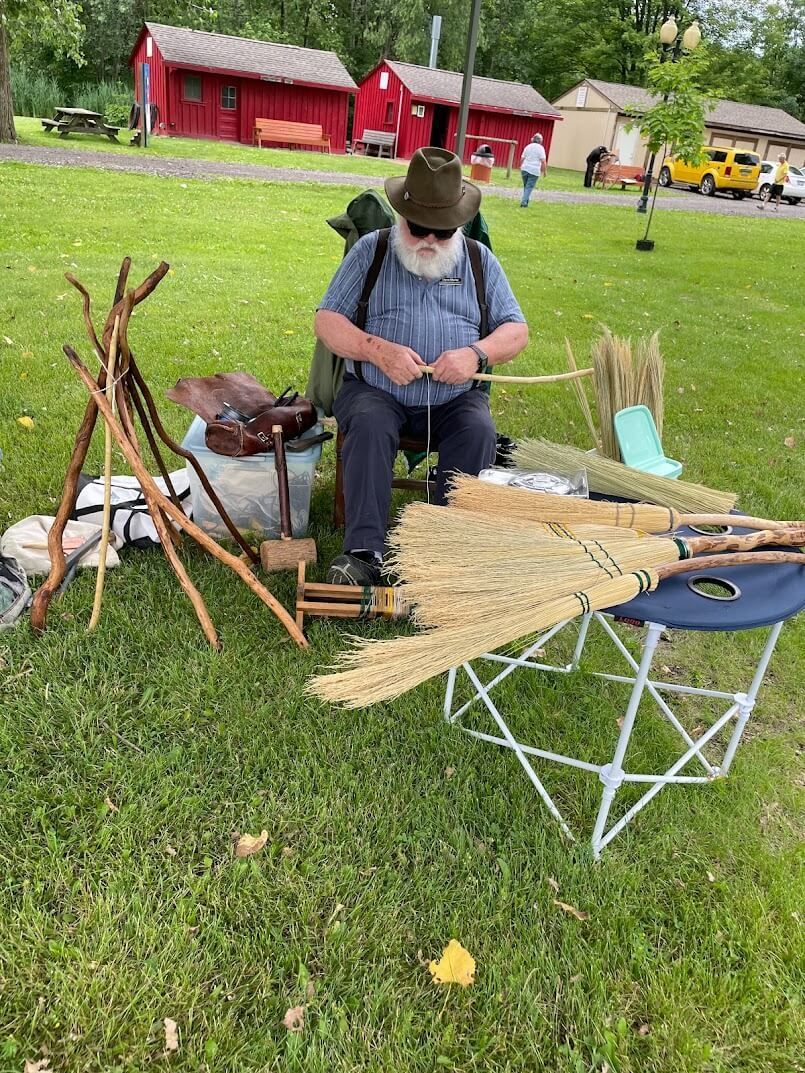 A man is sitting in the grass making a broom.