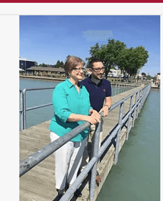 A man and a woman are standing on a dock overlooking a body of water.