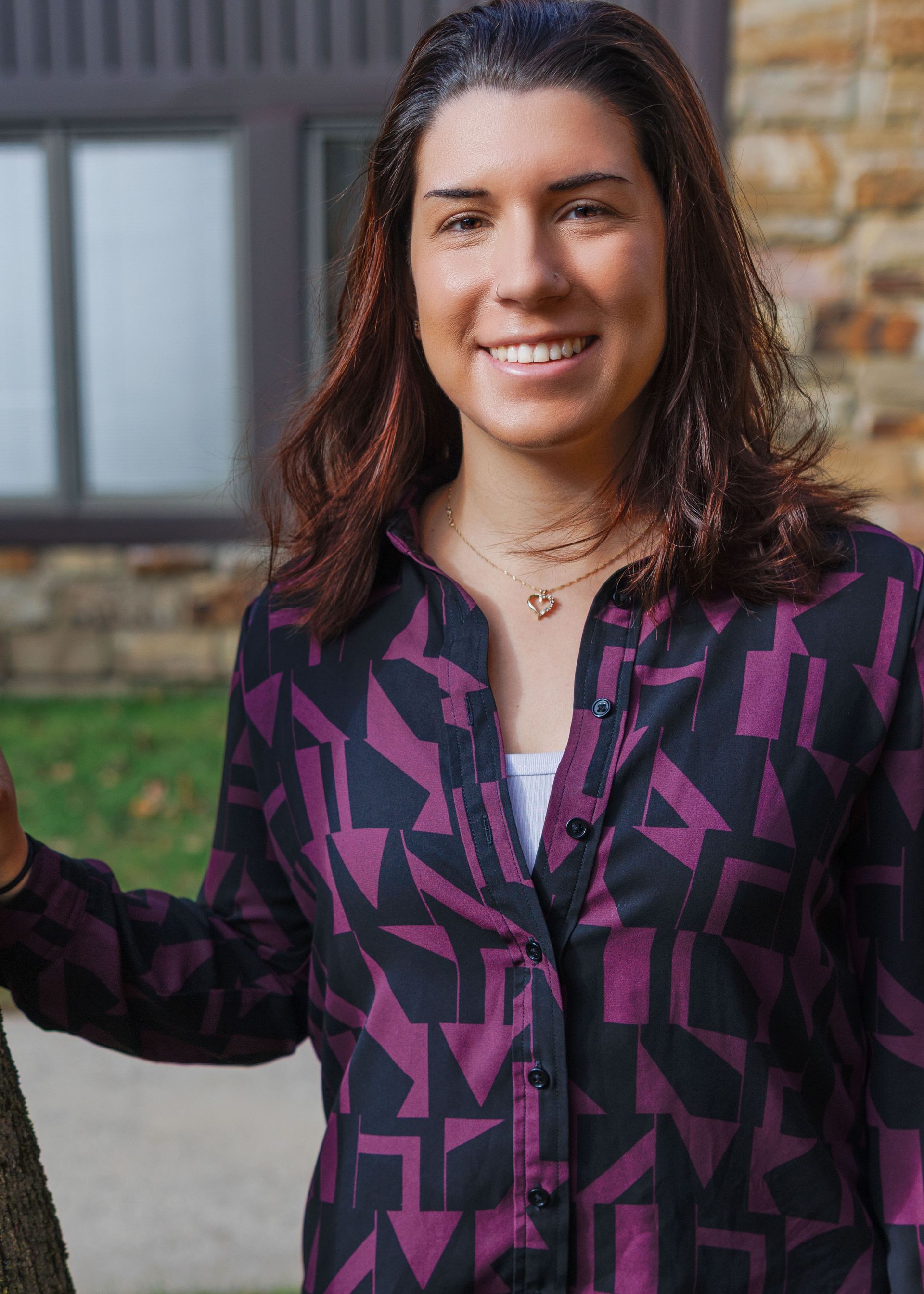 A woman in a black shirt is leaning against a tree and smiling.