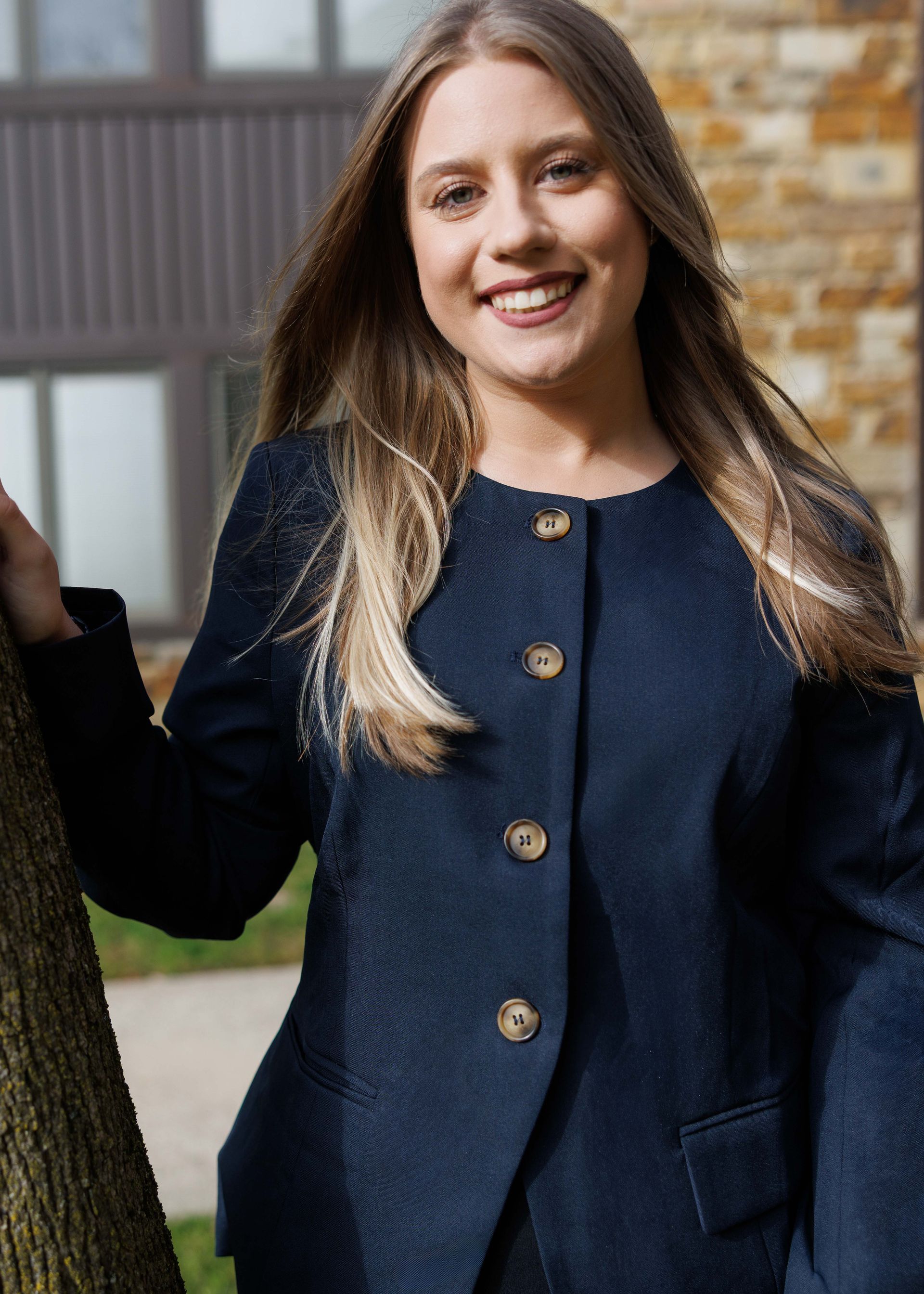 A woman in a black shirt is leaning against a tree and smiling.