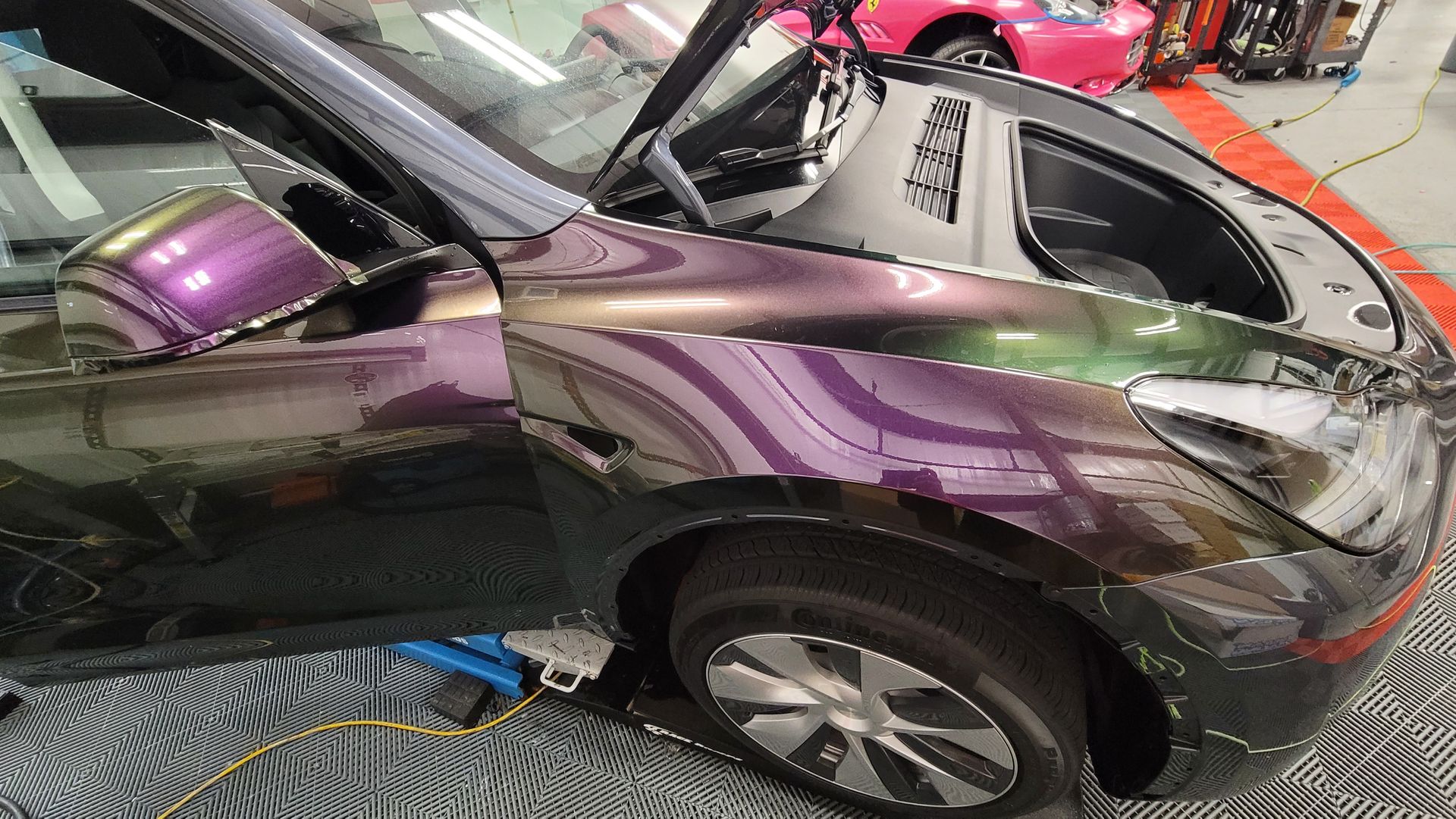 A purple tesla model s is parked in a parking lot in front of a building.