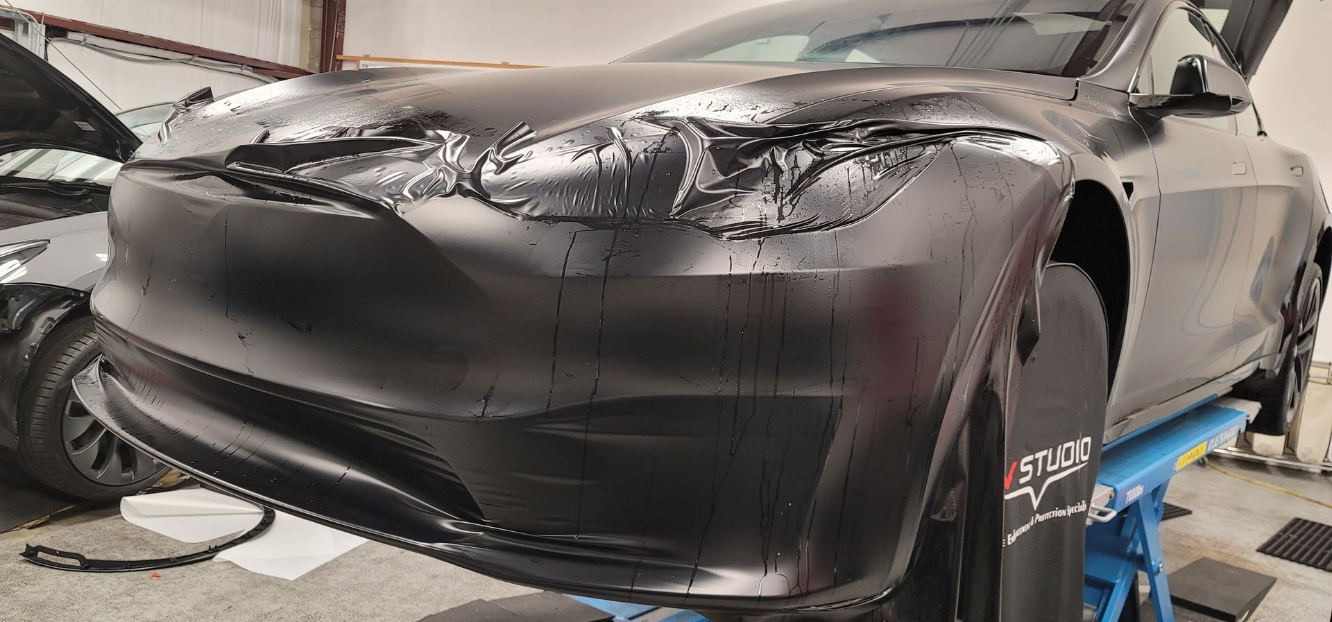 A black tesla model s is sitting on a lift in a garage.