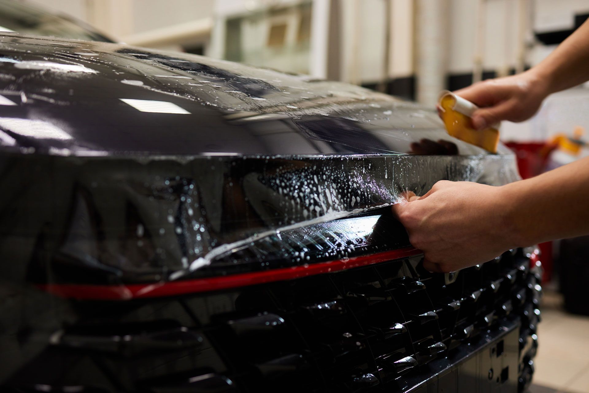 A person is applying a protective film to the hood of a car.