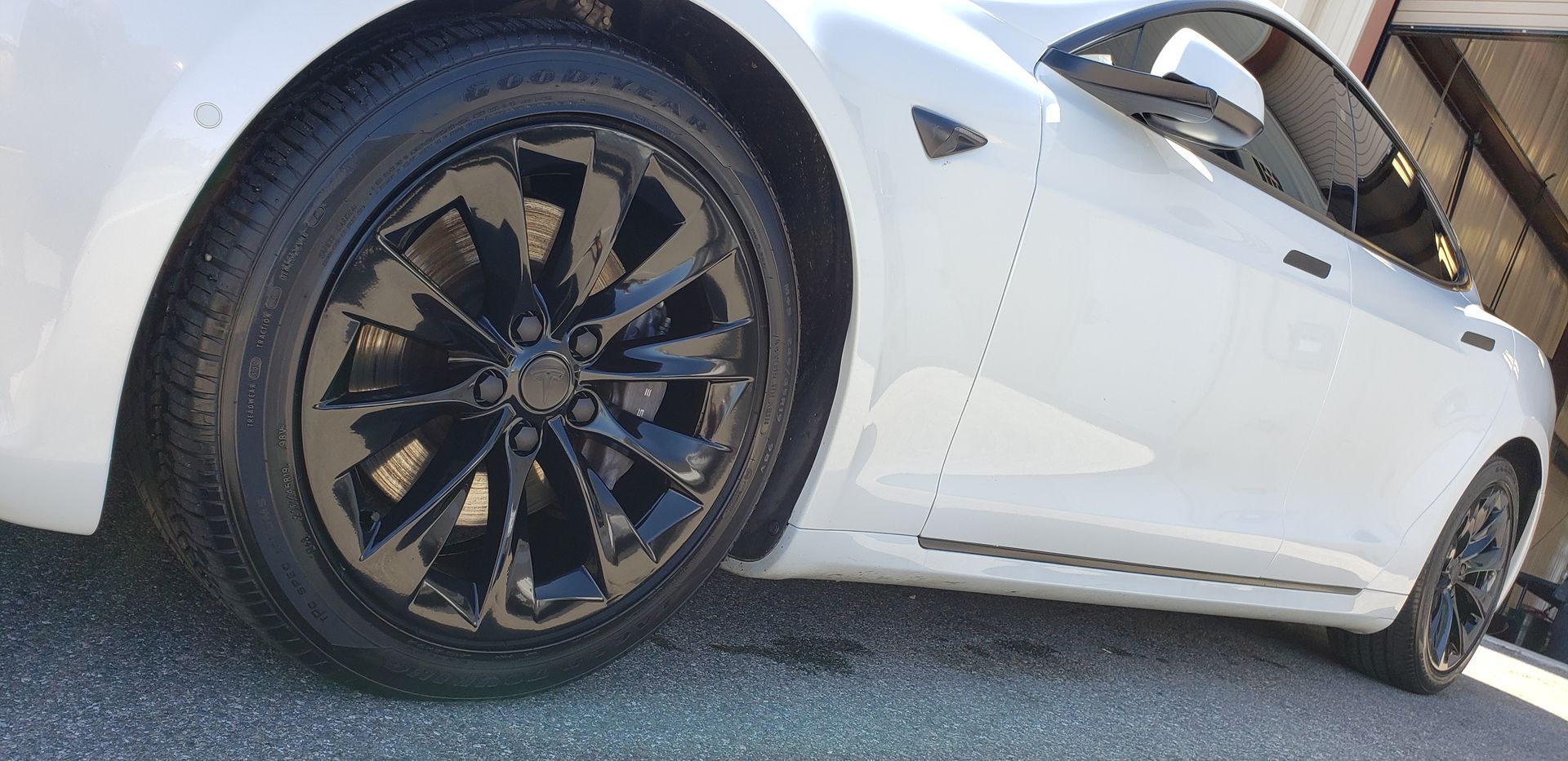 A white tesla model 3 with black wheels and tires is parked in front of a garage.