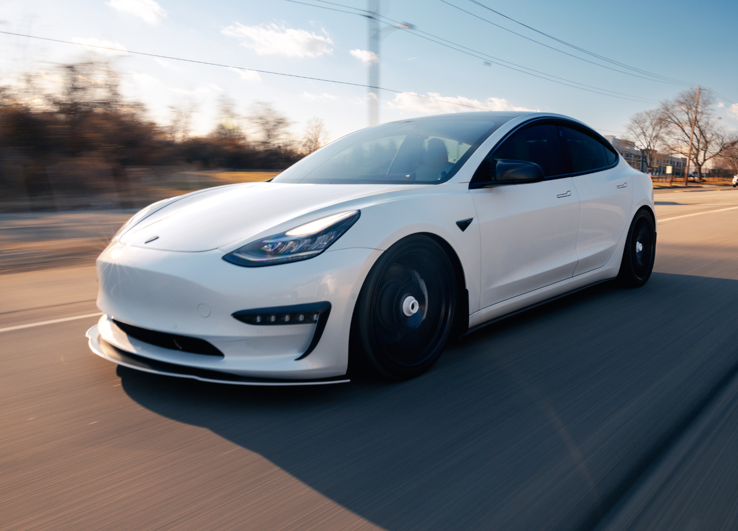 A white tesla model 3 is driving down a road.