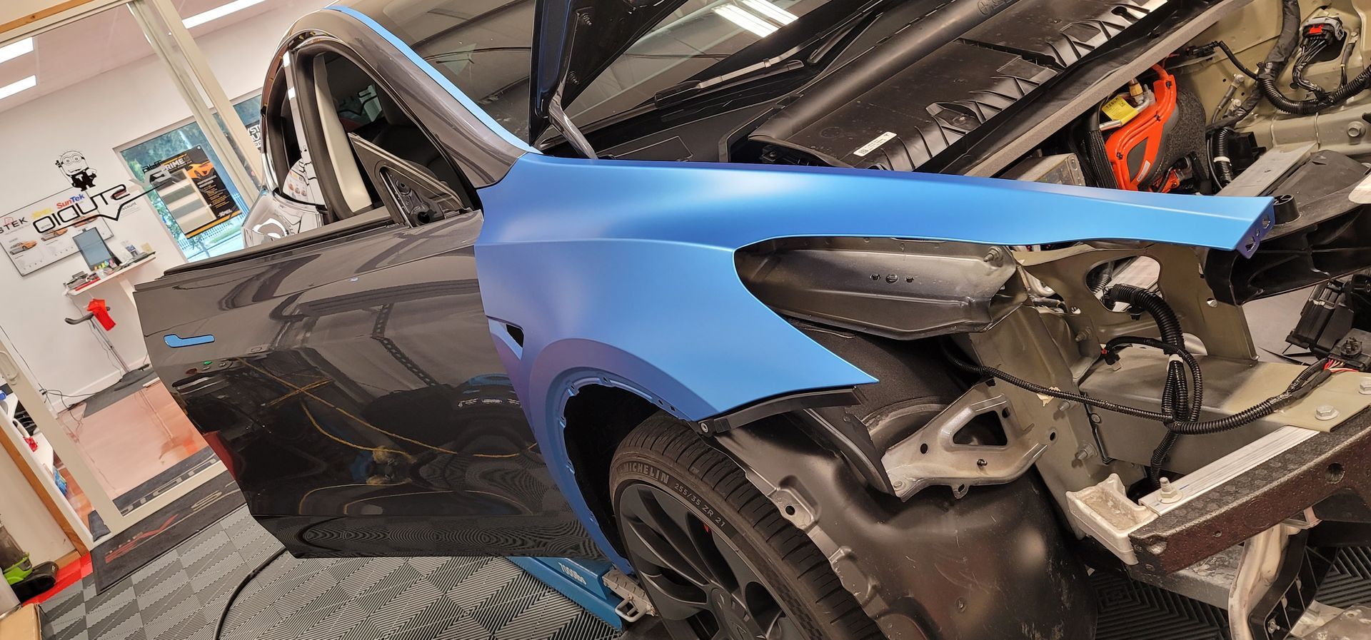 A blue tesla model 3 is parked in a garage.