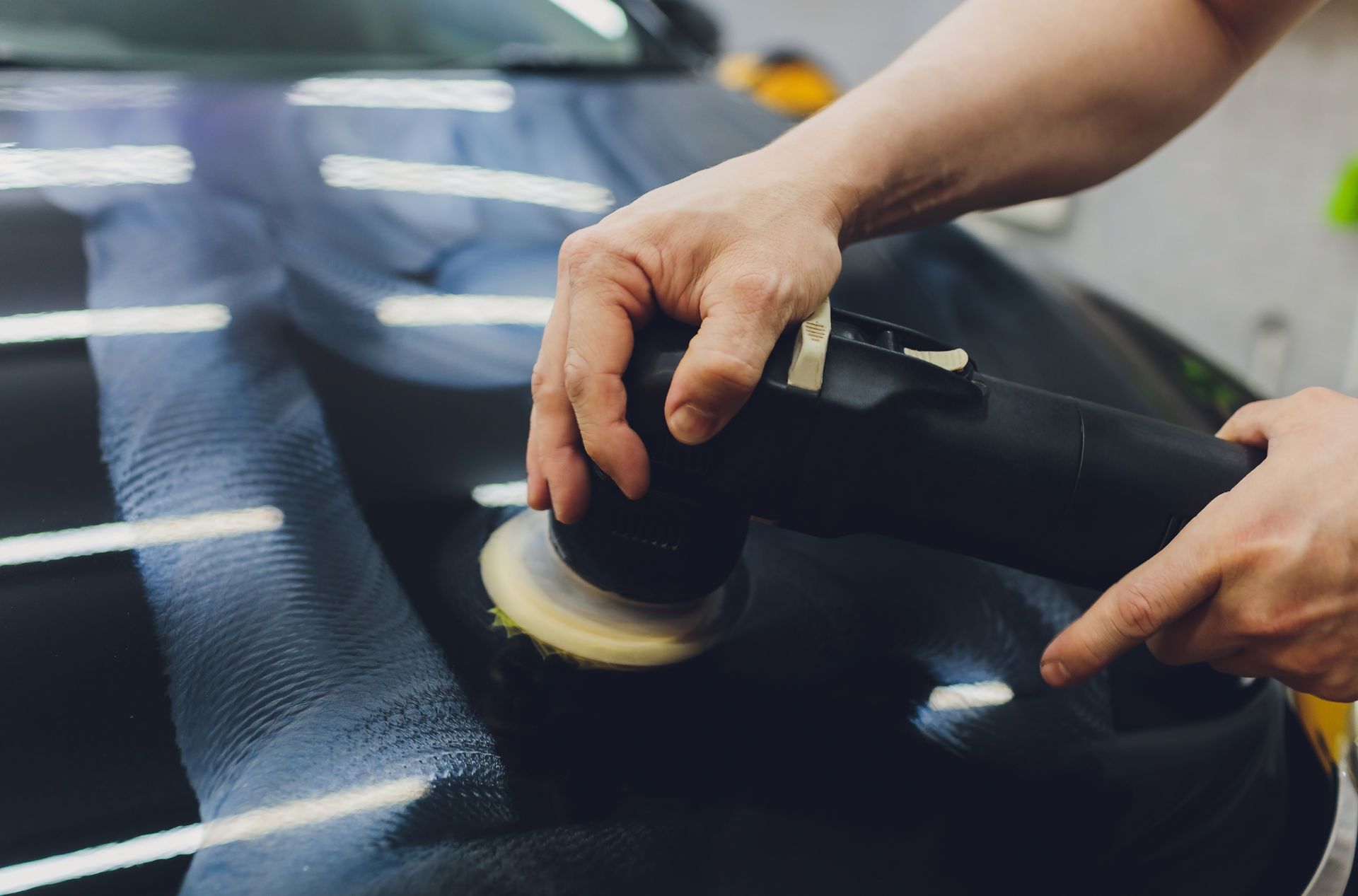 A person is polishing a black car with a machine.