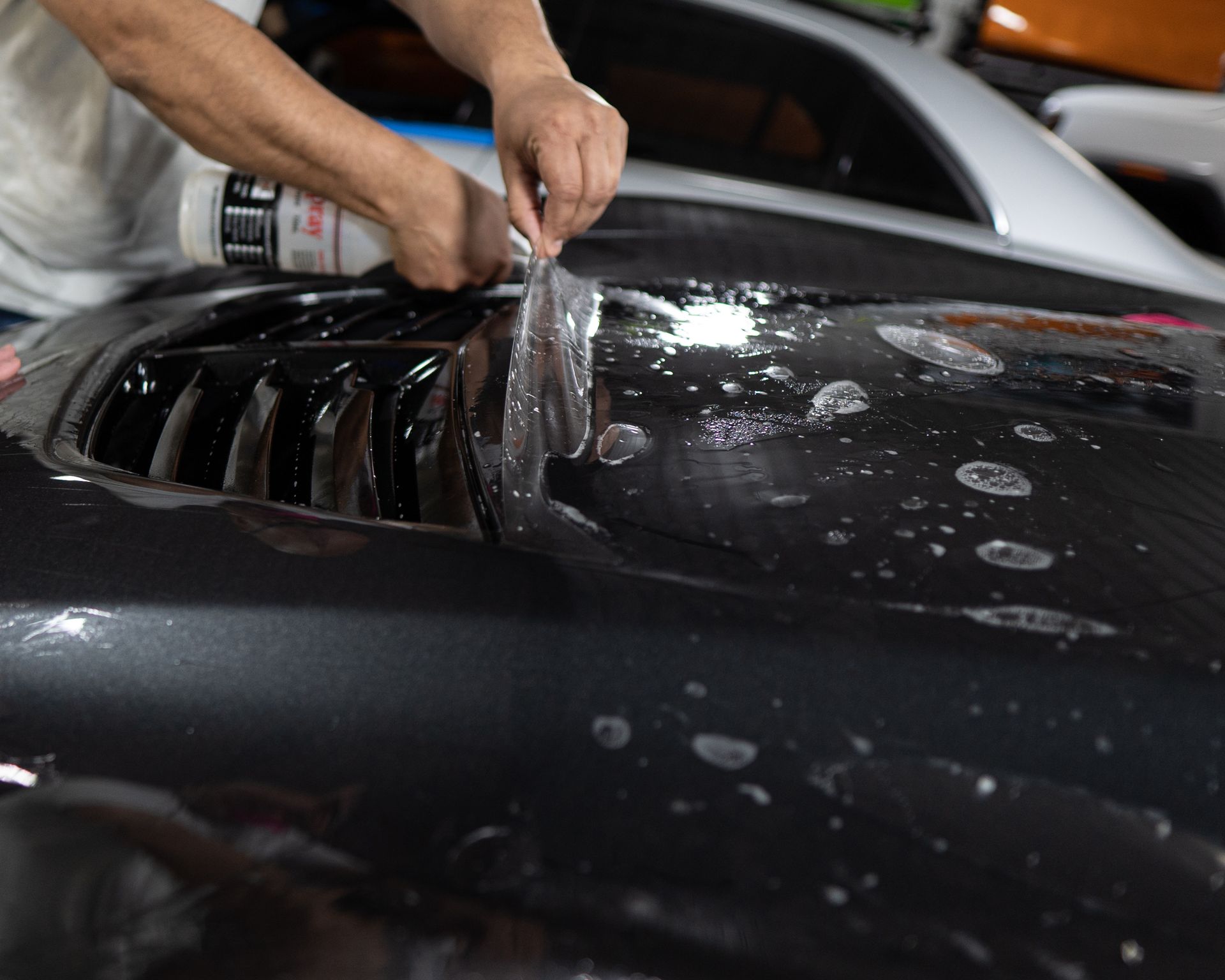 A man is applying a clear film to the hood of a car.