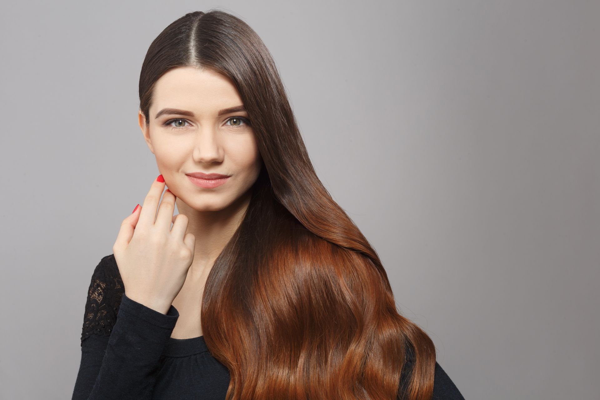 A woman with long hair is standing in front of a gray background.