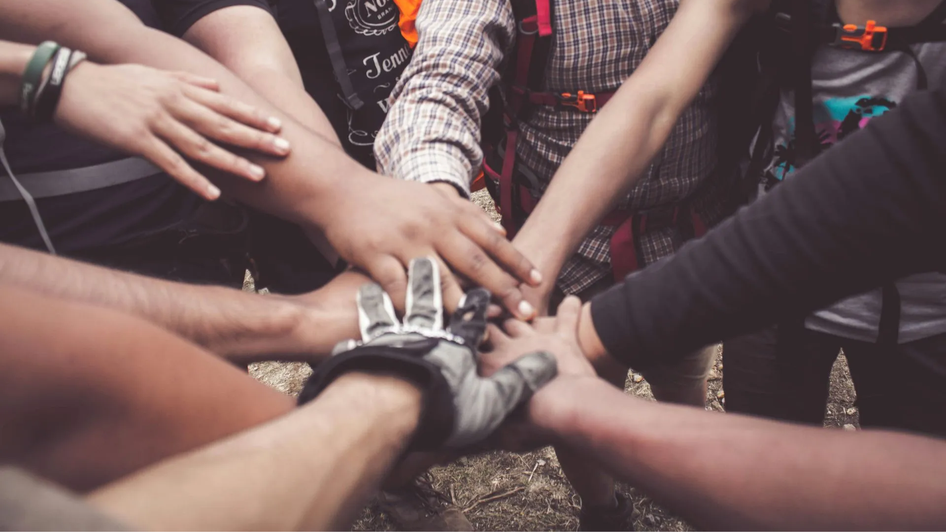 A close-up of a group of people stacking their hands together in a circle, signifying teamwork and unity outdoors.