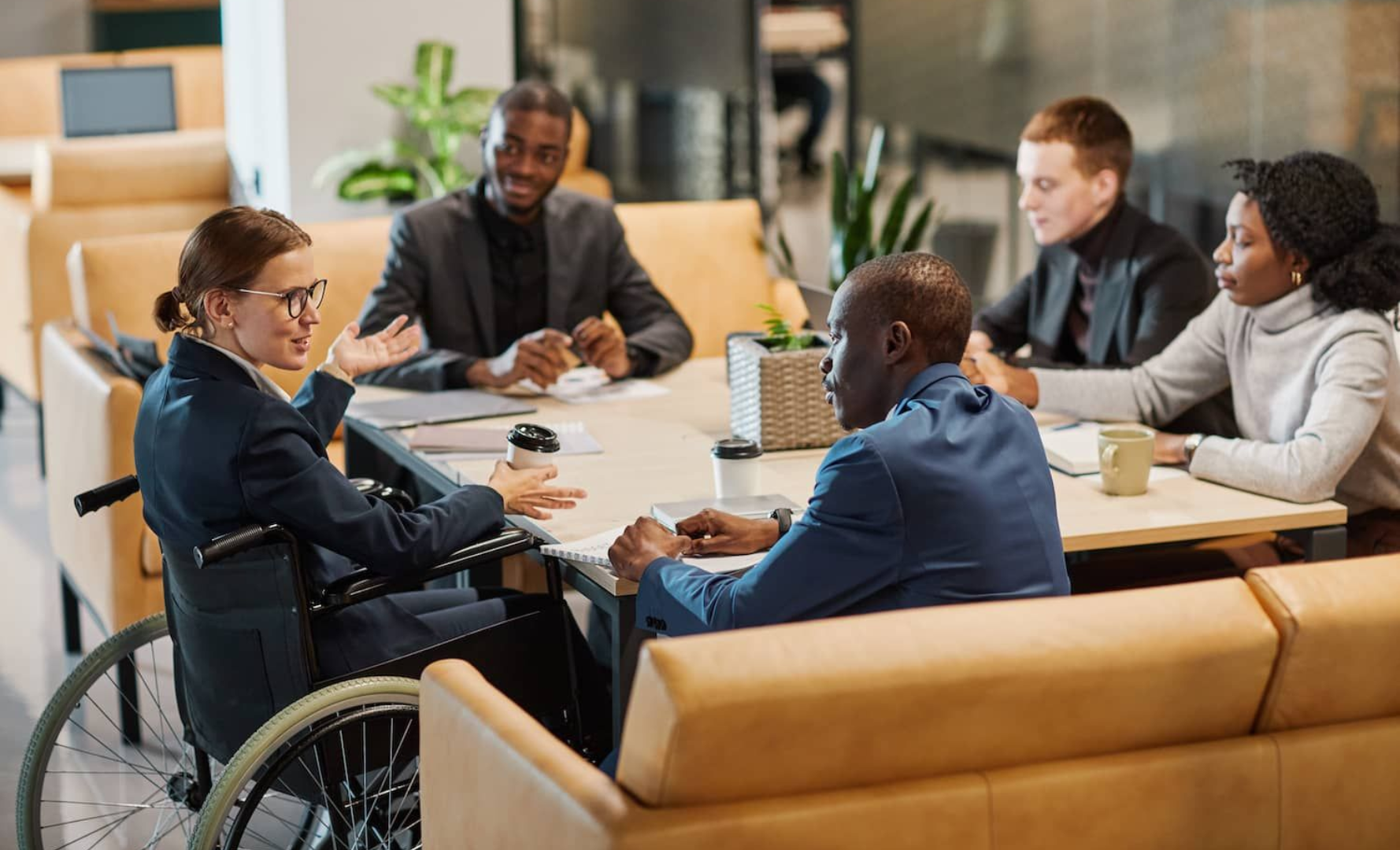 A diverse group of professional colleagues seated at a table in a modern office, engaged in a collaborative discussion.