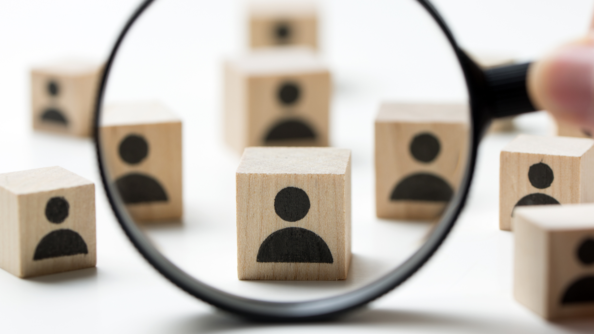 A magnifying glass focuses on a wooden block printed with a person icon, among several other similar blocks on a white surface.