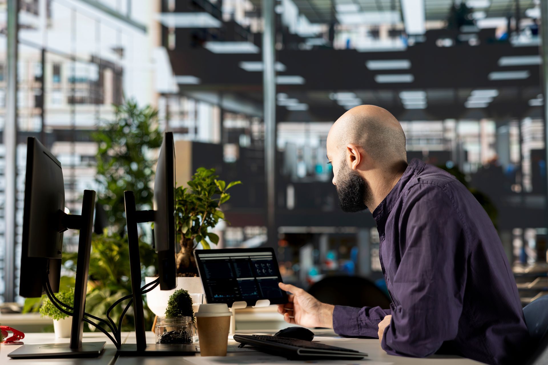 A person in a purple shirt works at a desk with two monitors and a tablet in a modern office.