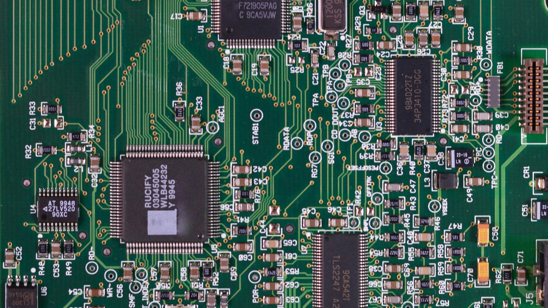 Close-up of a green printed circuit board featuring various integrated circuits, microchips, and electronic components.