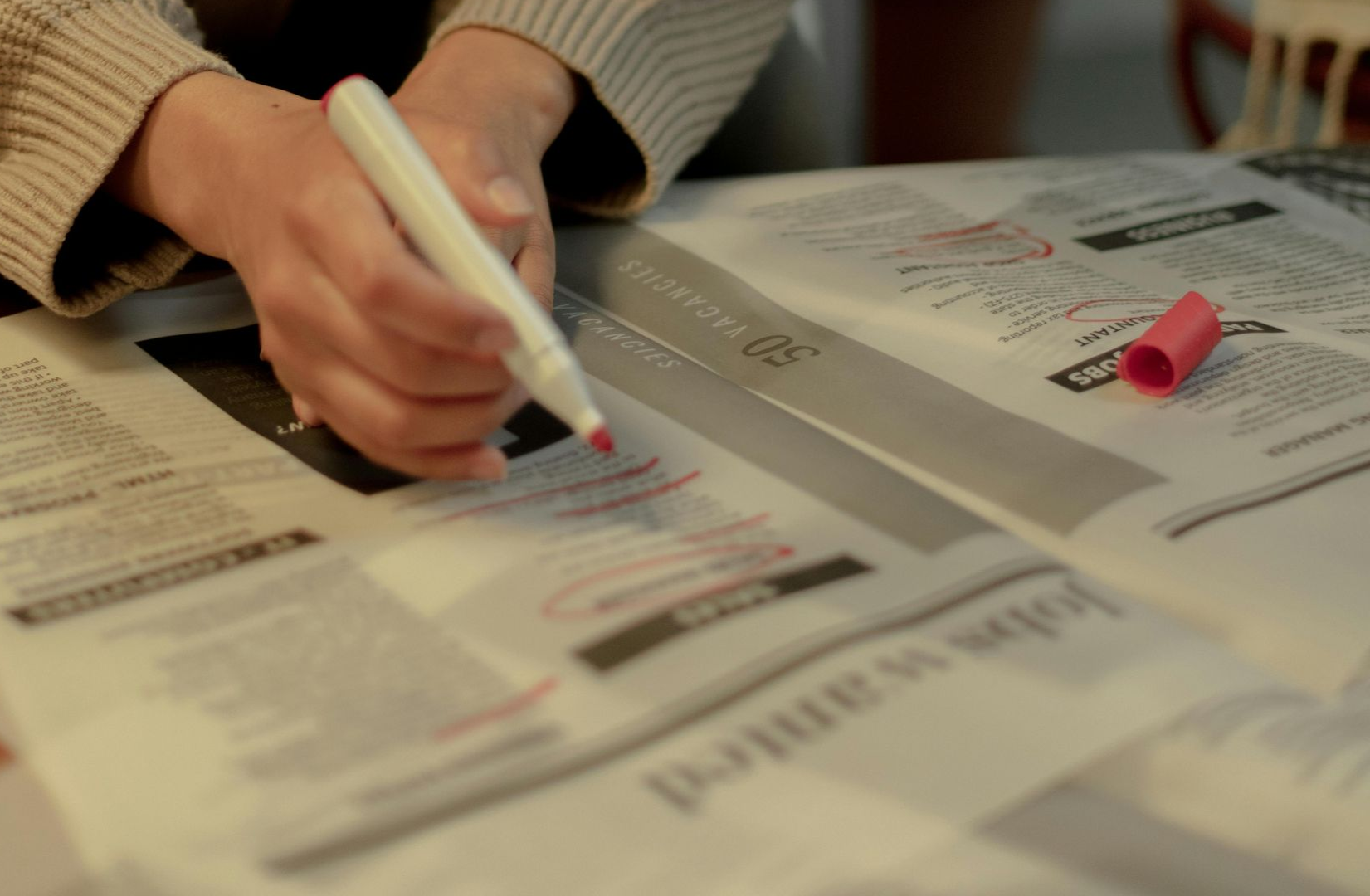 A person uses a red marker to circle job listings in a newspaper.