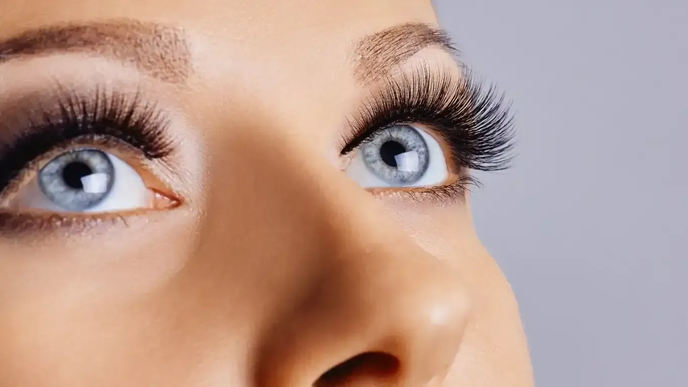 Close-up of light blue eyes with long, dark eyelashes after a lash lift, looking upwards.