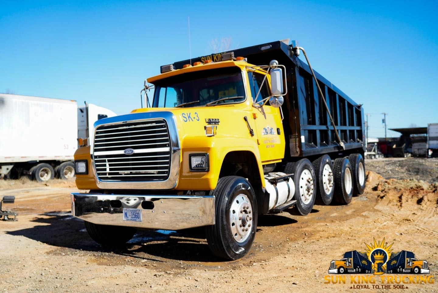 A yellow dump truck is parked in a dirt field.