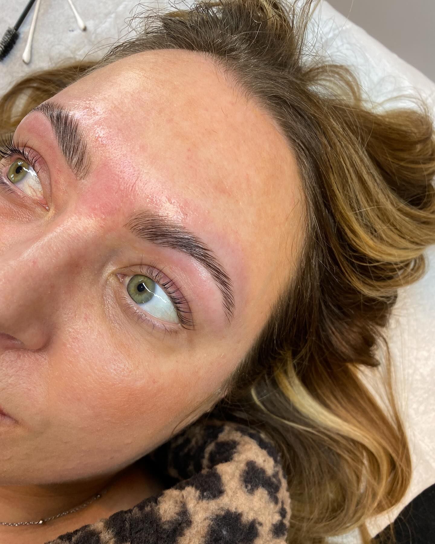 Woman with newly tattooed eyebrows; light brown skin, green eyes.