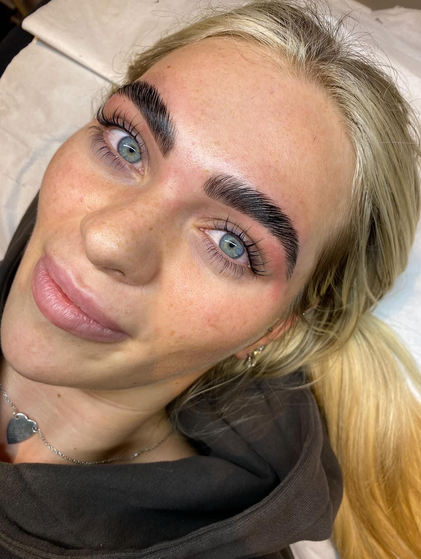 Woman with freshly-done, dark eyebrows; lying on a white surface, looking at the camera.