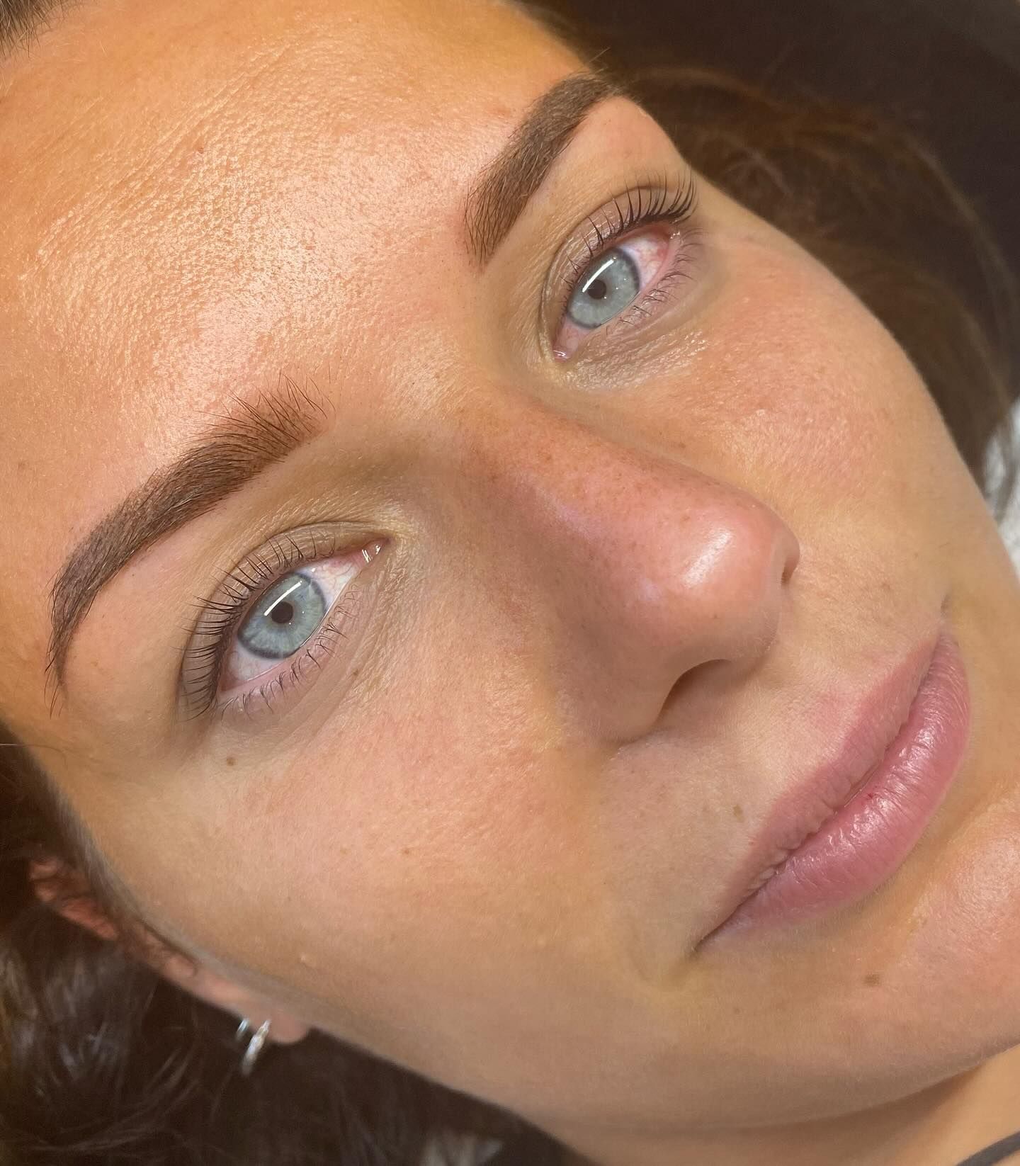 Woman with blue eyes, eyebrow tattoo, soft brown brows, and neutral expression.