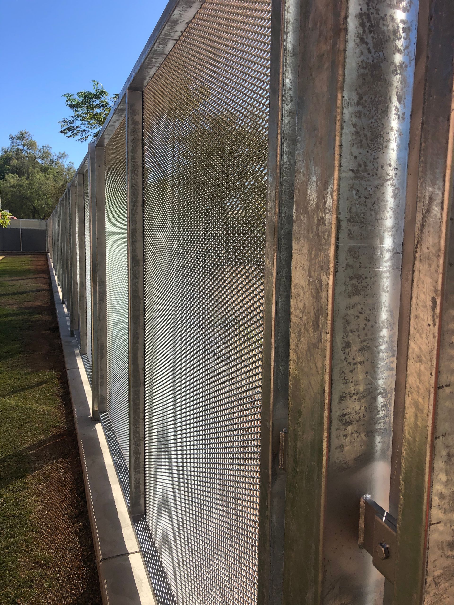 A close up of a metal fence with a wooden fence in the background.