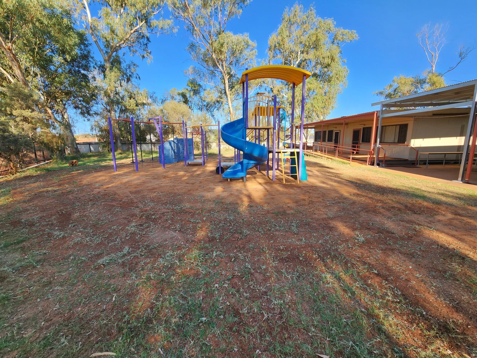 A playground with a blue slide , swings , and a yellow roof.