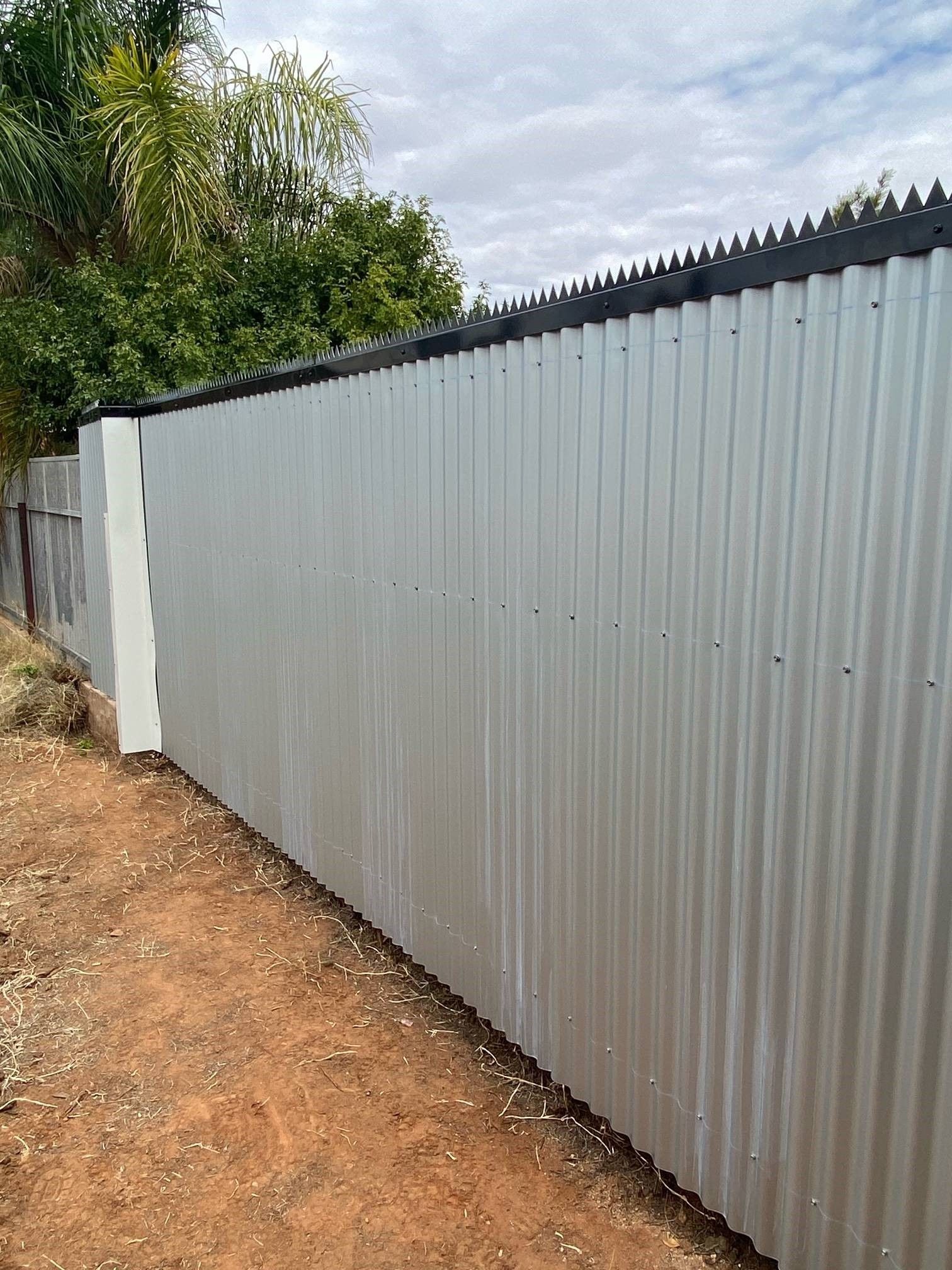 A metal fence with barbed wire on it is surrounded by dirt and trees.