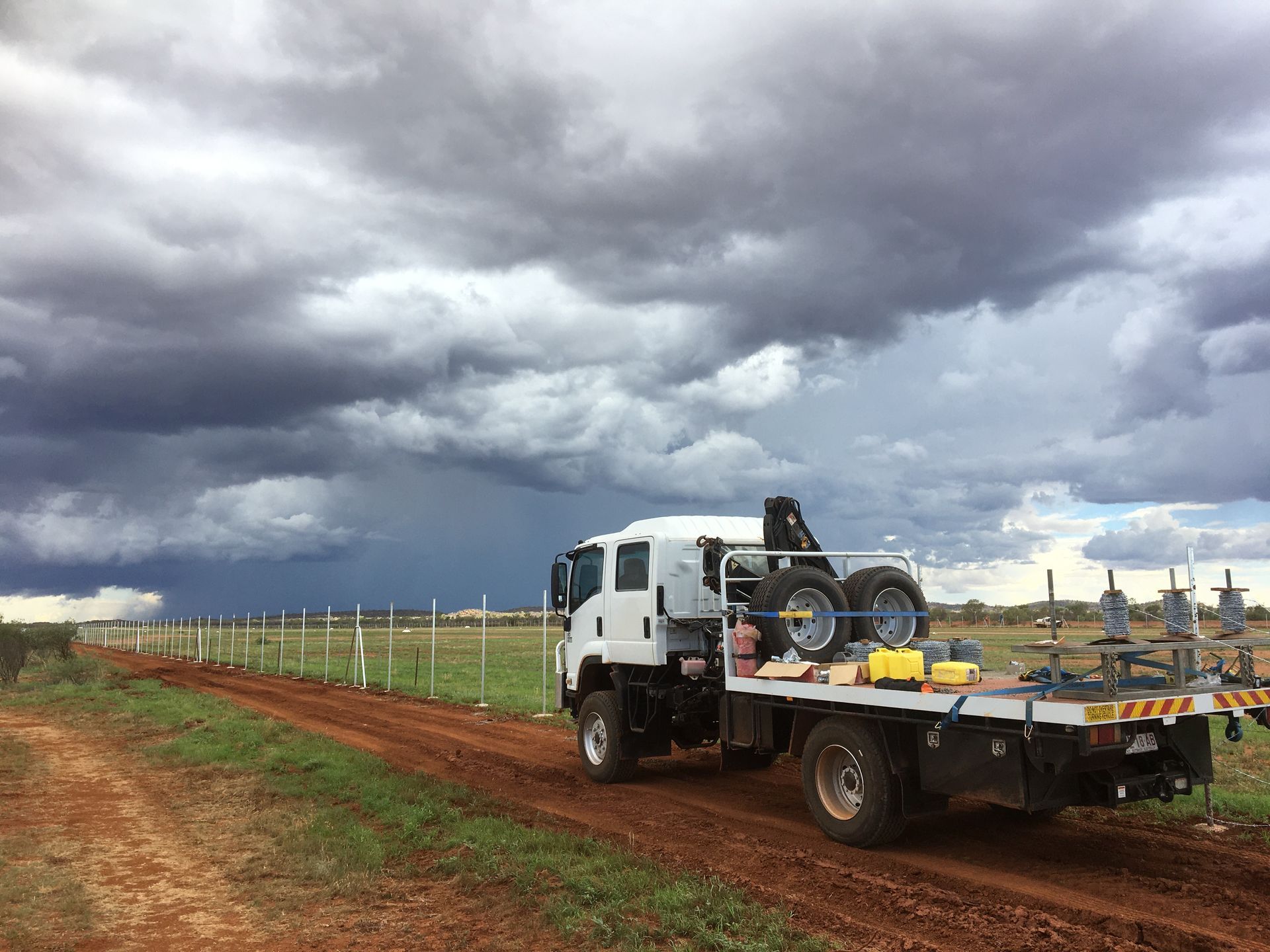 A white truck with a crane on the back is parked on a dirt road.