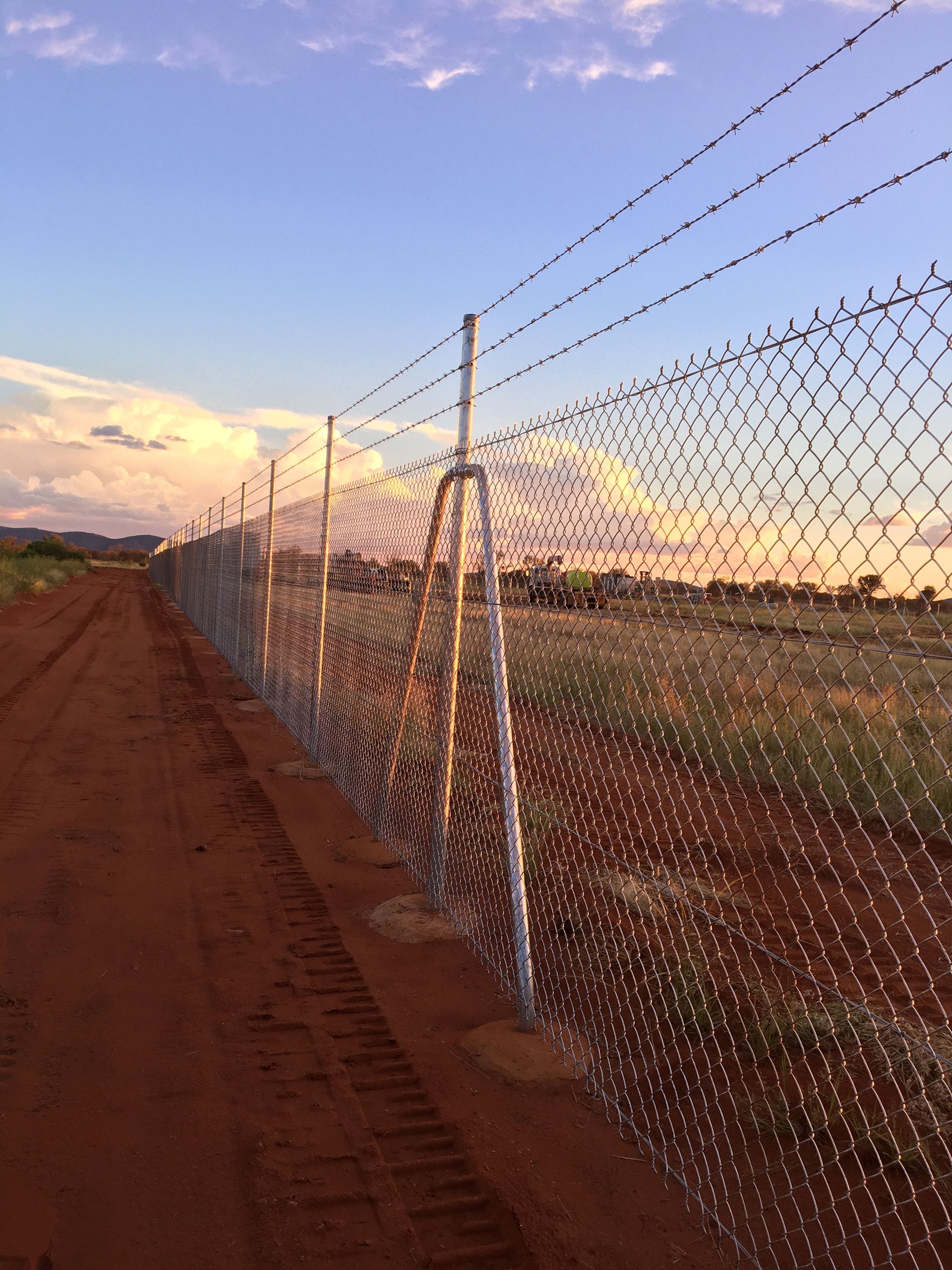 A chain link fence is along the side of a dirt road.