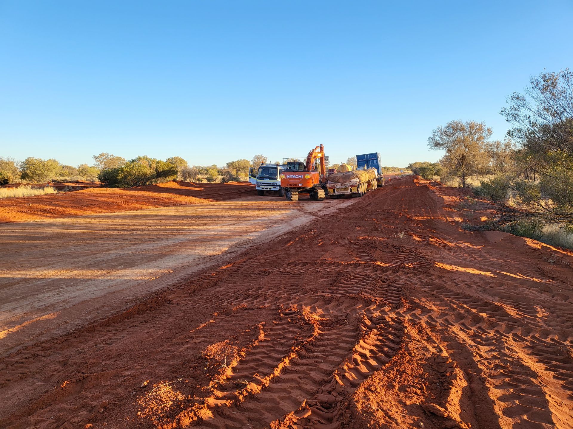 A truck is driving down a dirt road next to a bulldozer.
