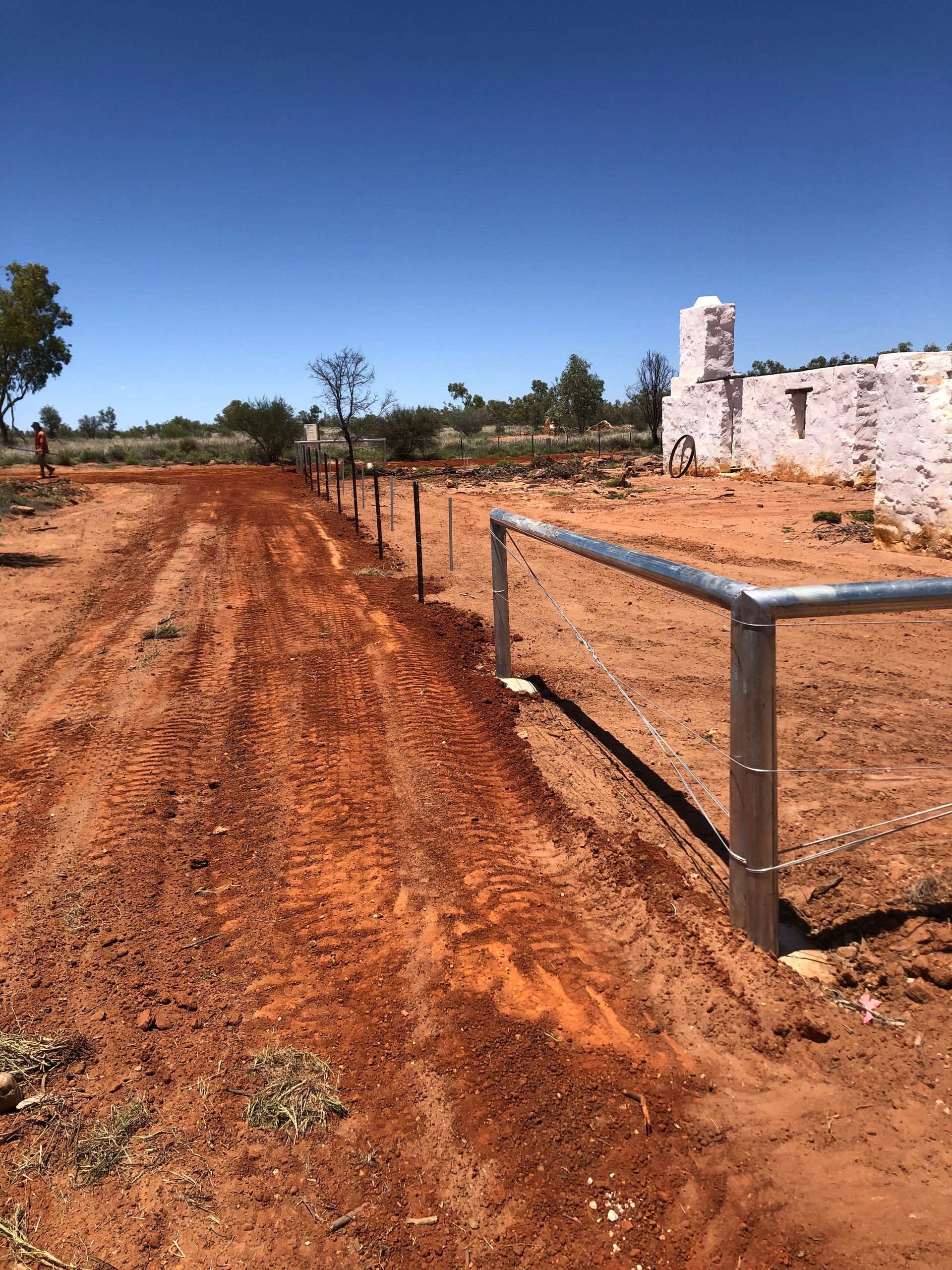 A dirt road with a fence and a building in the background.