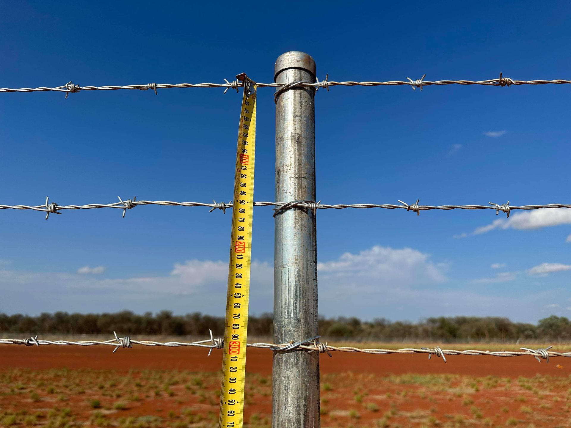 A tape measure is being used to measure the height of a barbed wire fence.