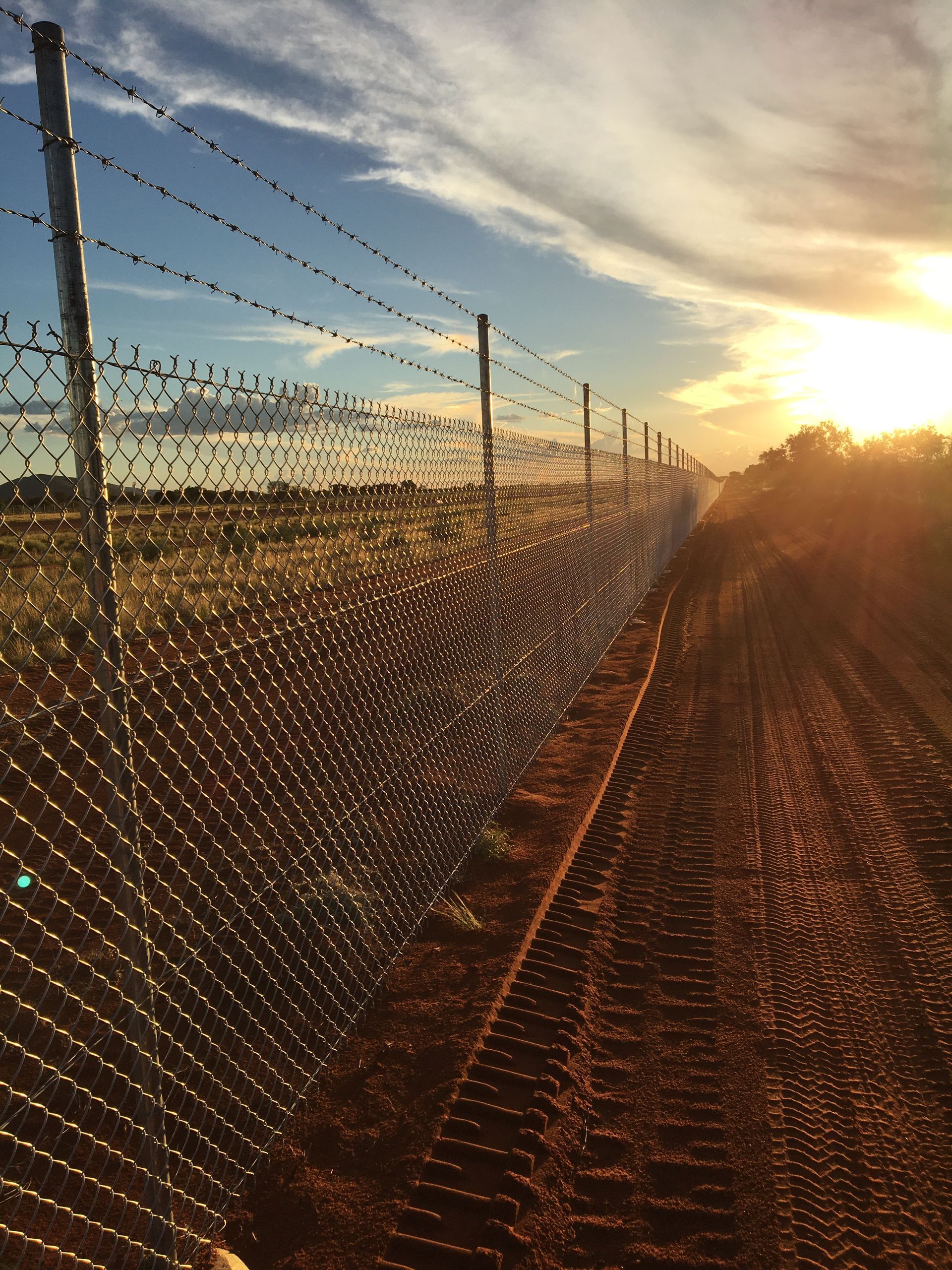 A barbed wire fence surrounds a dirt road at sunset