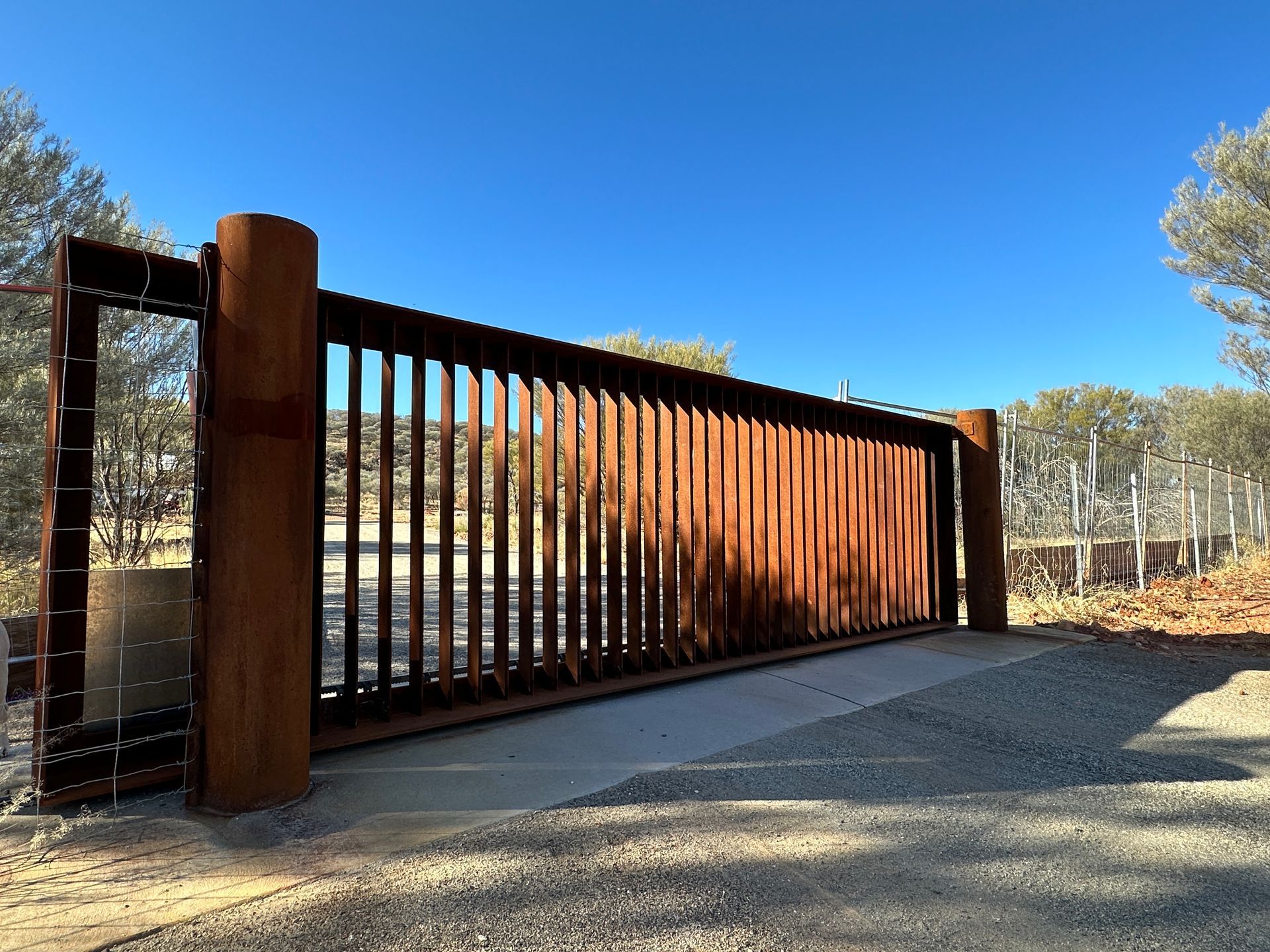 A rusty metal gate is sitting on top of a gravel road.