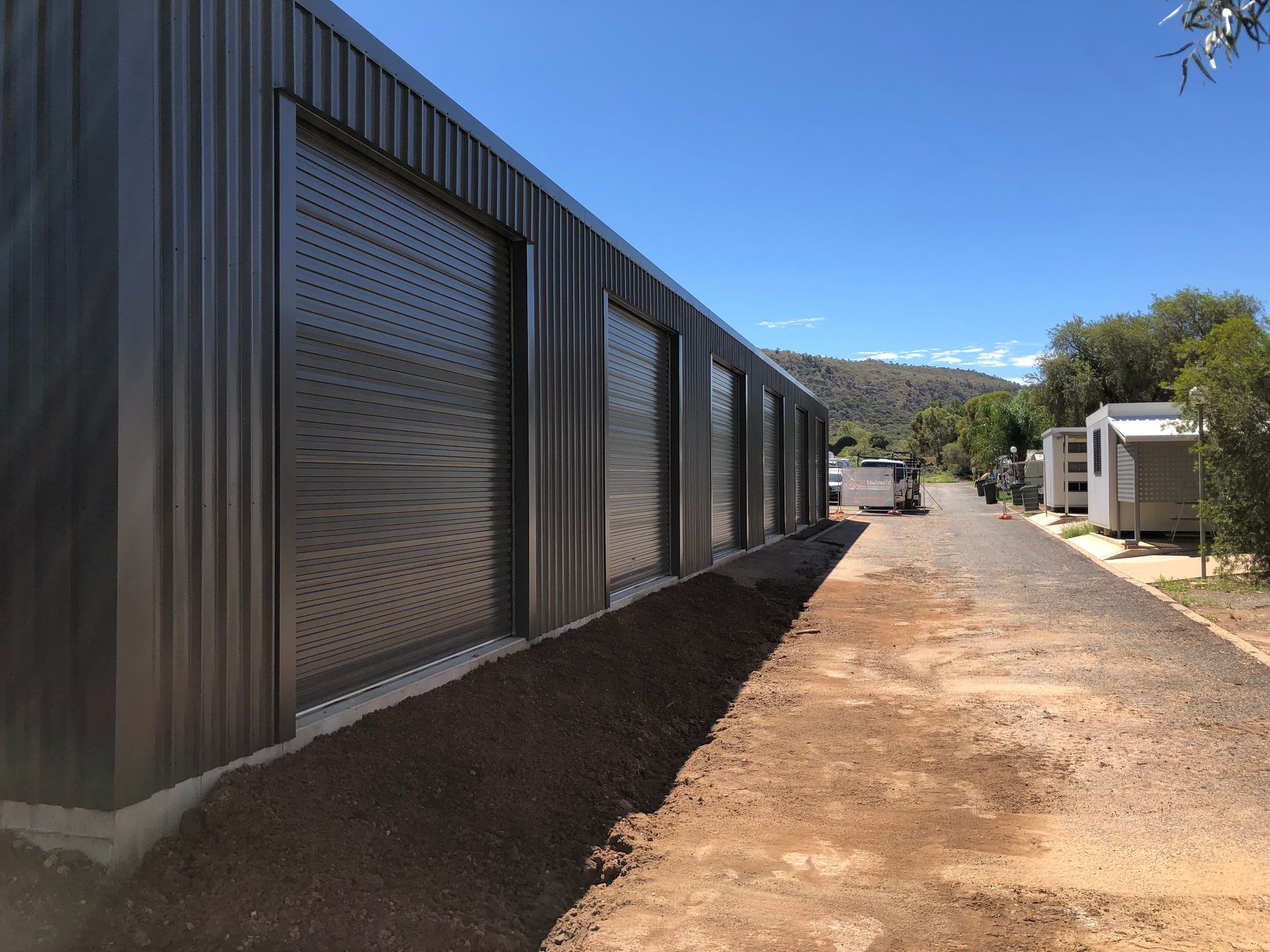 Gray metal building with shuttered doors on a gravel path under a blue sky.