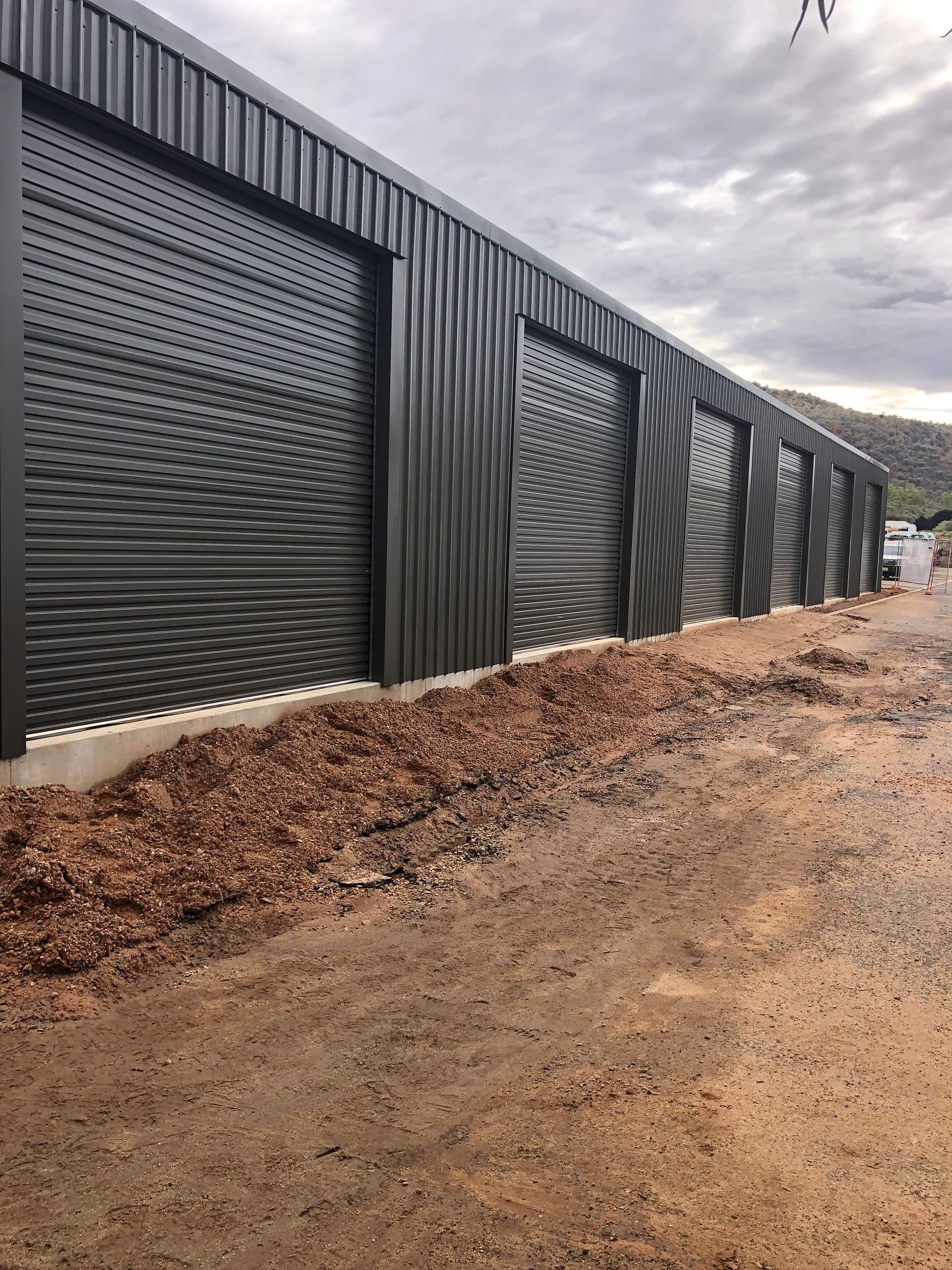 Dark gray corrugated metal building with large patterned sliding doors on a gravel driveway.