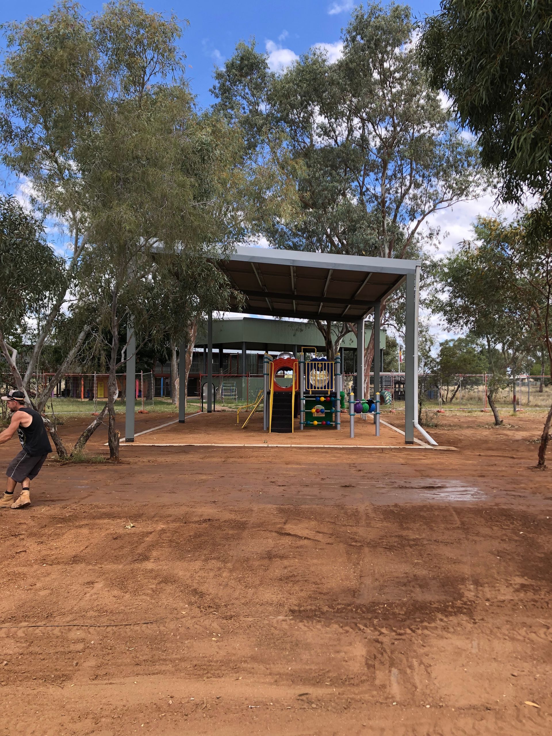 A man is standing in a dirt field in front of a playground.