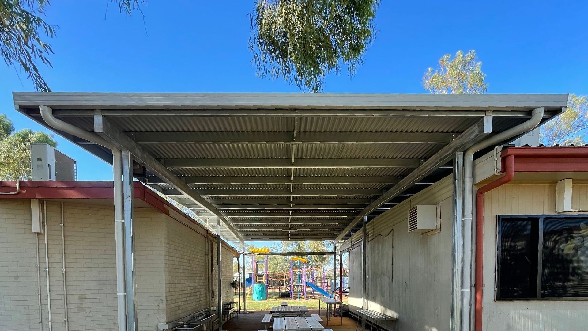 A covered walkway between two buildings with a blue sky in the background.