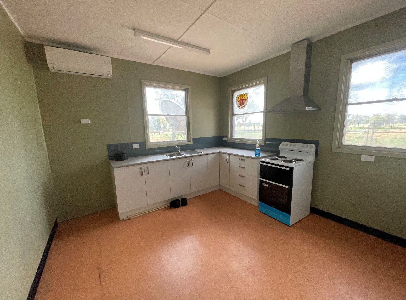 An empty kitchen with a stove , sink , and two windows.