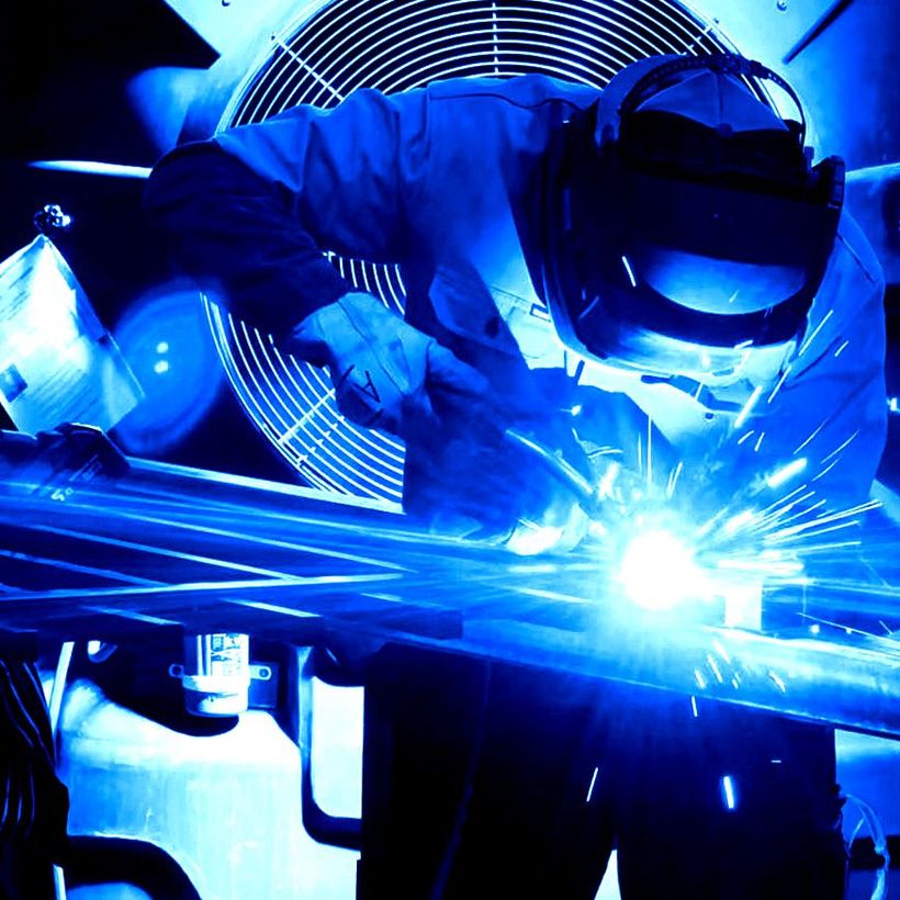 A man wearing a welding mask is welding a piece of metal