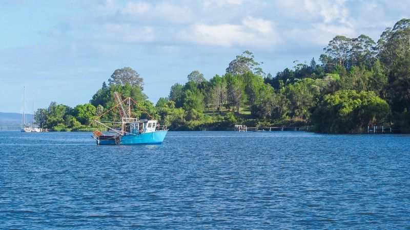 Blue Fishing Boat on a Blue Lake, With Green Trees — Mid North Coast Solar Carports in Maclean, NSW
