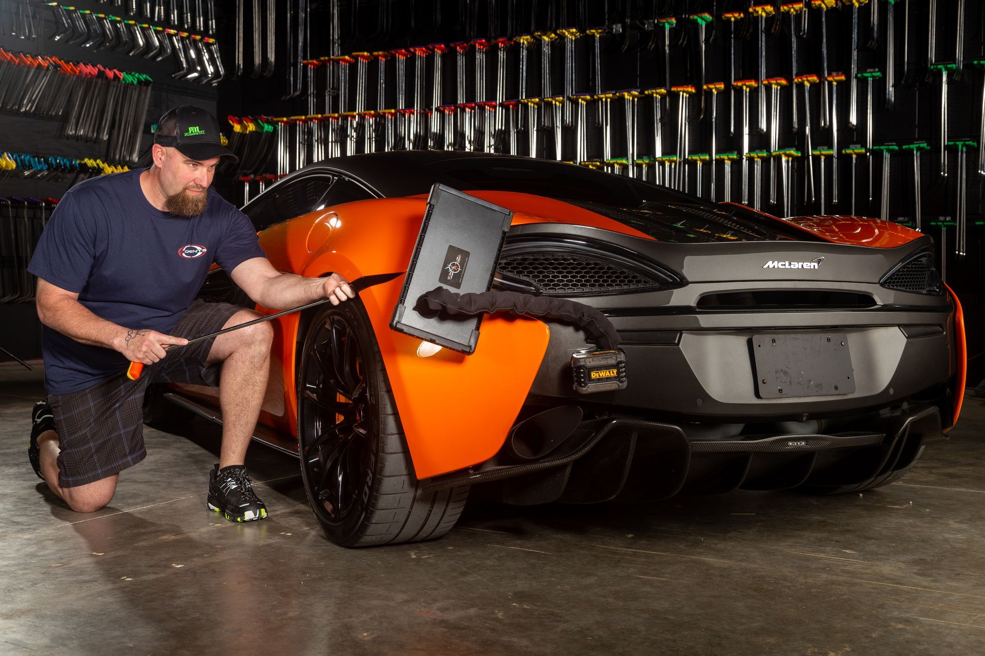 Paintless Dent Repair (PDR) technician massaging metal from behind the panel on an orange car