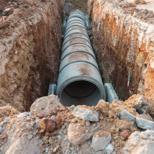 A large concrete pipe is being installed in a trench