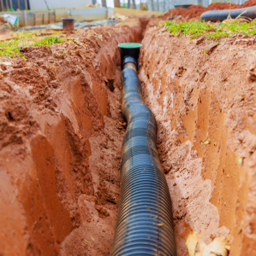 A black pipe is being installed in a trench in the dirt.