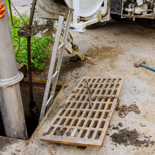 A manhole cover is being removed by a vacuum truck.
