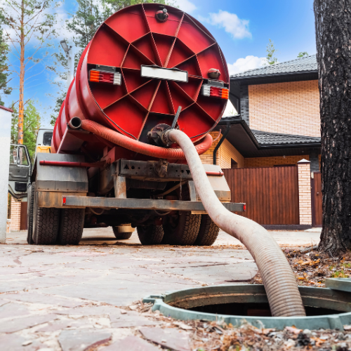 A red truck with a hose attached to it is pumping water into a manhole.