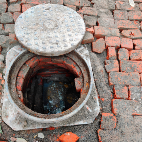 A manhole cover is open on a brick sidewalk
