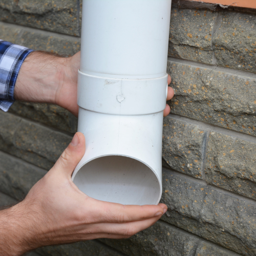 A person is holding a white pipe against a brick wall.